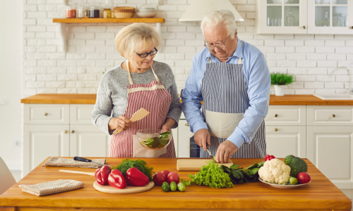 an older couple cooks a minimalist meal together, using simple ingredients and techniques, one of the many benefits of the Minimalist lifestyle.